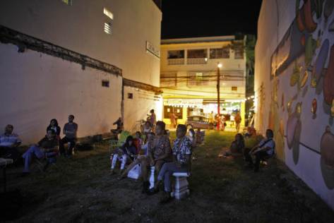 In this Sept. 21, 2014 photo, people watch a movie at a makeshift outdoor movie theater in the Santurce neighborhood in San Juan, Puerto Rico. Outdoor movie nights are held in an empty lot in a spot named Cinema Paradiso created by filmmaker Michelle Malley Campos. (AP Photo/Ricardo Arduengo)